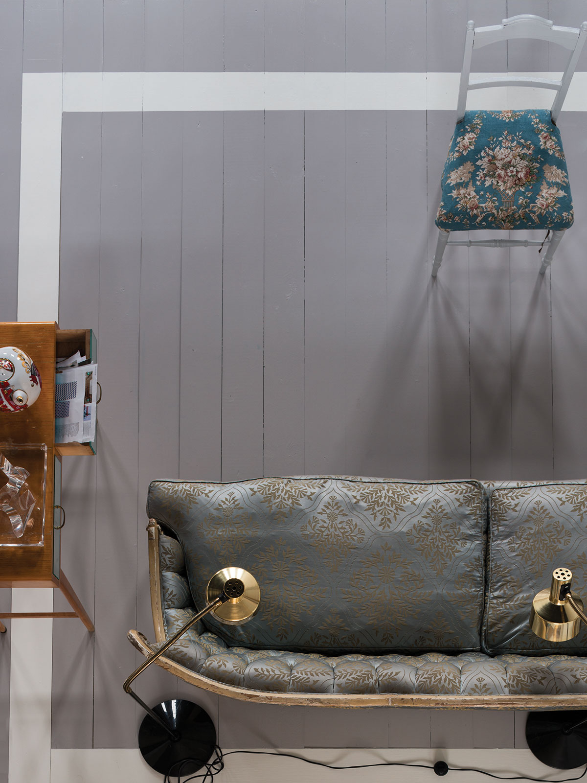 An aerial view of a strong blue grey painted wooden floor, contrasting with a sofa upholstered in a traditional pattern of soft blue with weathered gold detailing.