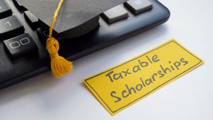 graduation cap on corner of laptop, with yellow sign that reads, 