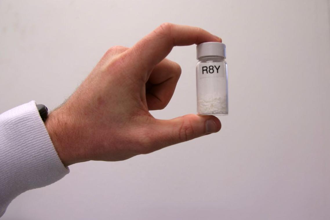 Man's hand holding a drug vial labelled R8Y up to the camera.