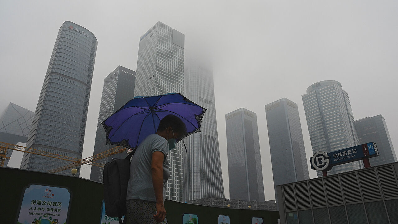 A pedestrian walks with an umbrealla on an overcast day in Beijing.
