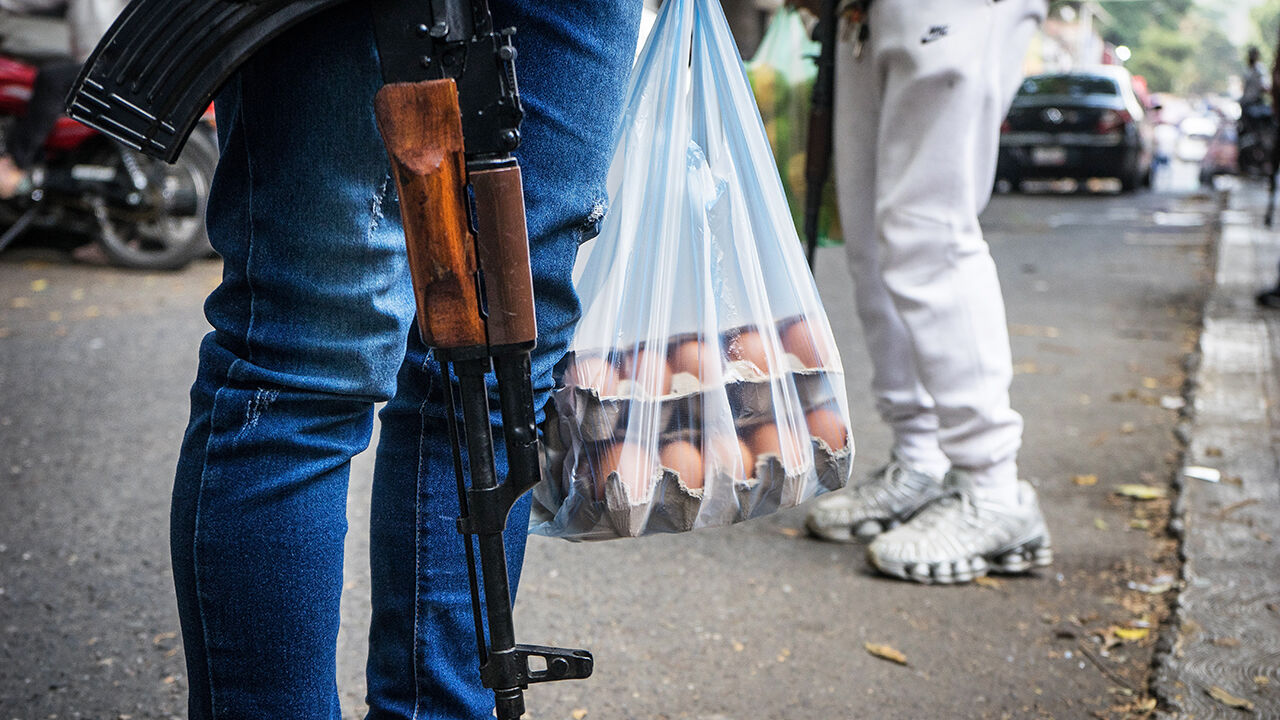 A member of an armed group stands holding a rifle and bag of eggs, as armed groups patrol markets in Caracas, Venezuela.