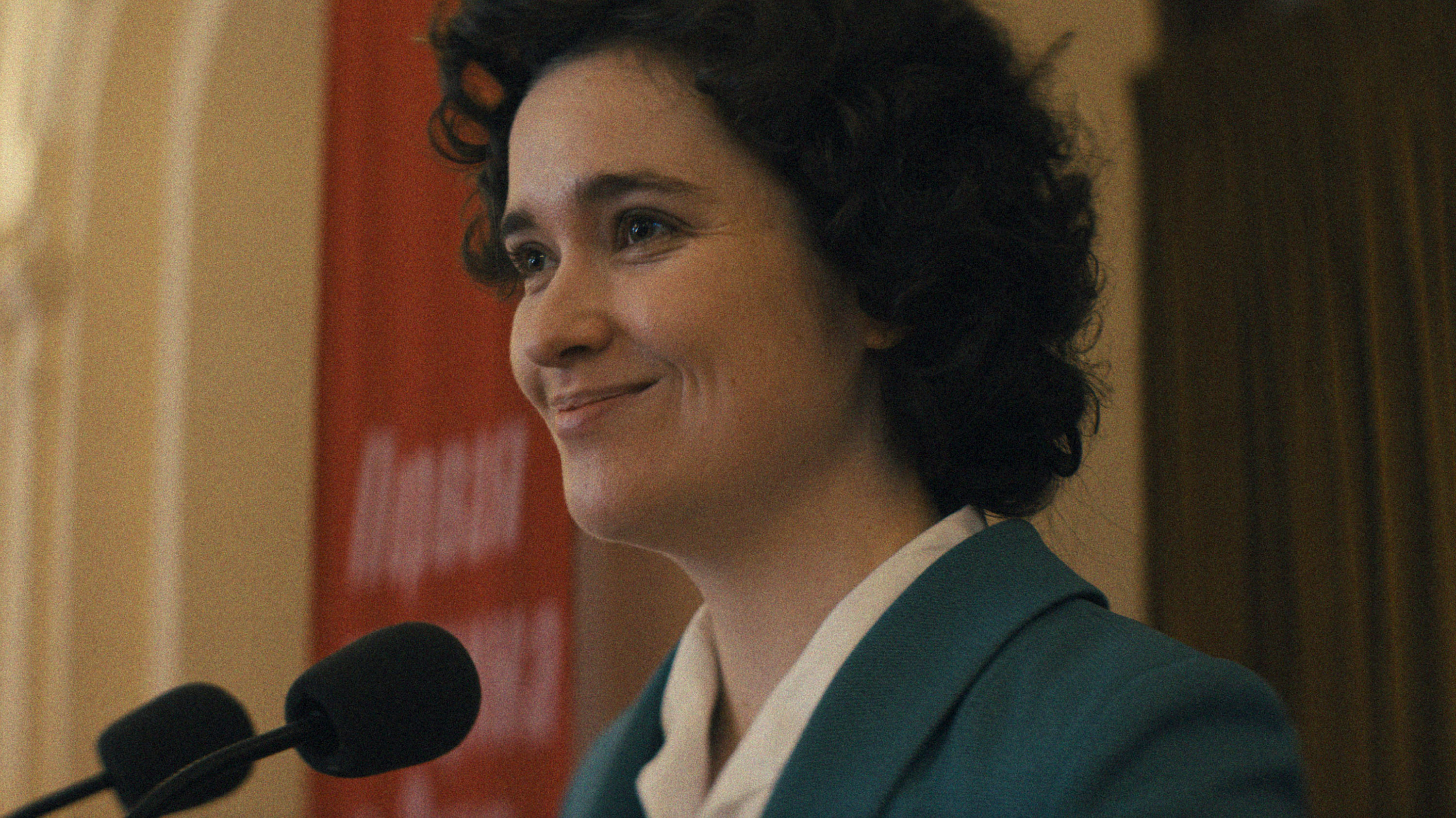 A woman smiles while speaking into a microphone.