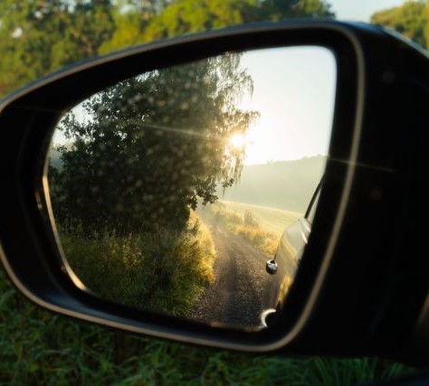 Car sideview mirror reflecting a sunlit stretch of road.