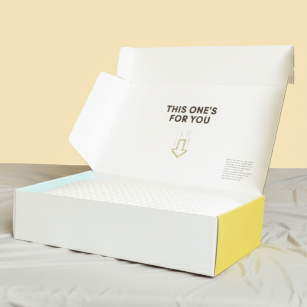 A white pillow inside a partially yellow and white open shipping box with the text 'THIS ONE'S FOR YOU' printed on the inner lid.