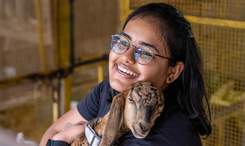 A smiling young woman holds a baby goat against her cheek inside an animal shelter.