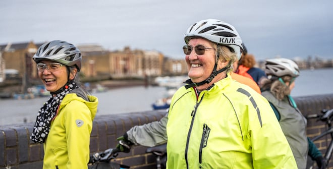 A Breeze Champion with other riders, wearing hi vis. There is a river and city-scape in the background.