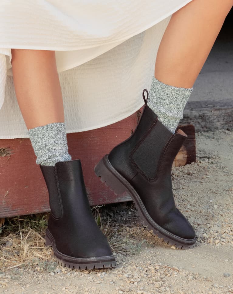 Girl standing on gravel, wearing a dress, grey socks and Salt Creek boot in Dark Chocolate