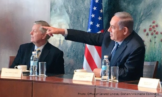 Senator Lindsey Graham sitting at a desk, pointing at something.