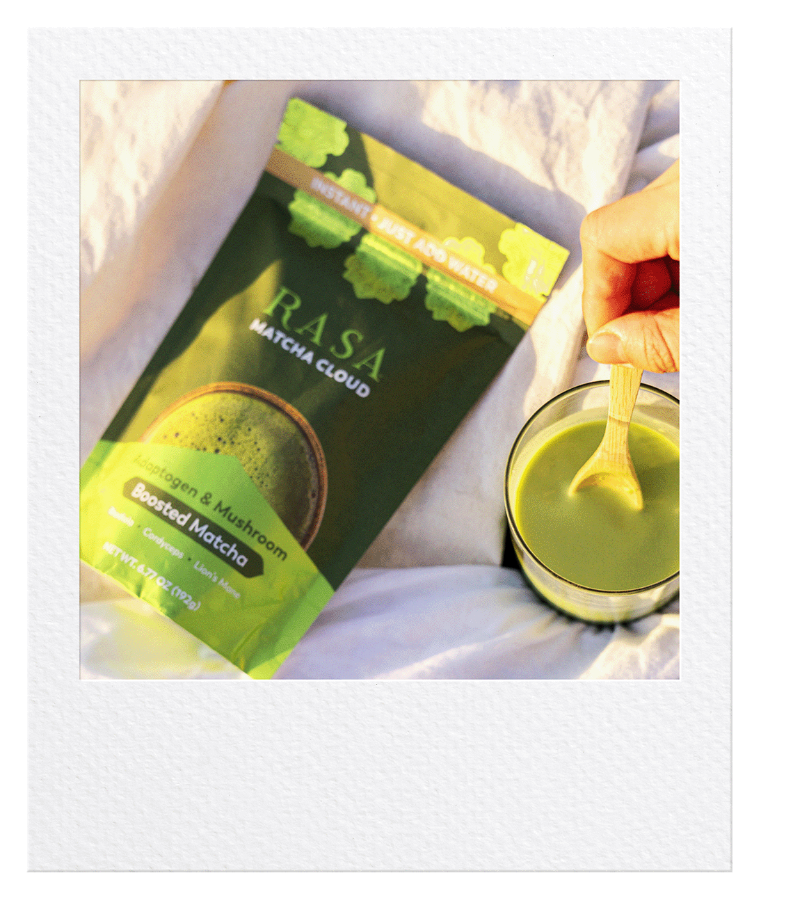 A polaroid picture of a bag of Matcha Cloud on a blanket while a hand stirs a freshly made cup of lively looking Matcha Cloud. 