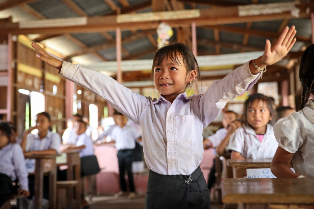 A girl in school smiling with arms outstretched.