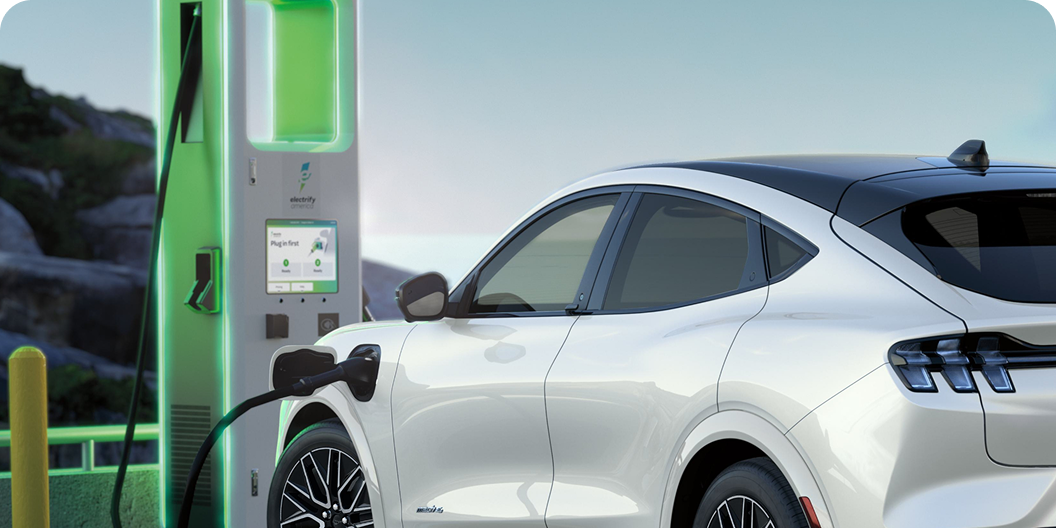 A white Ford vehicle charging at an illuminated green electric station