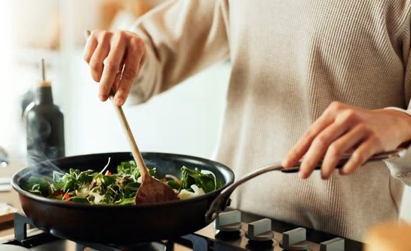 A person stirs a pan of vegetables with a wooden spoon.