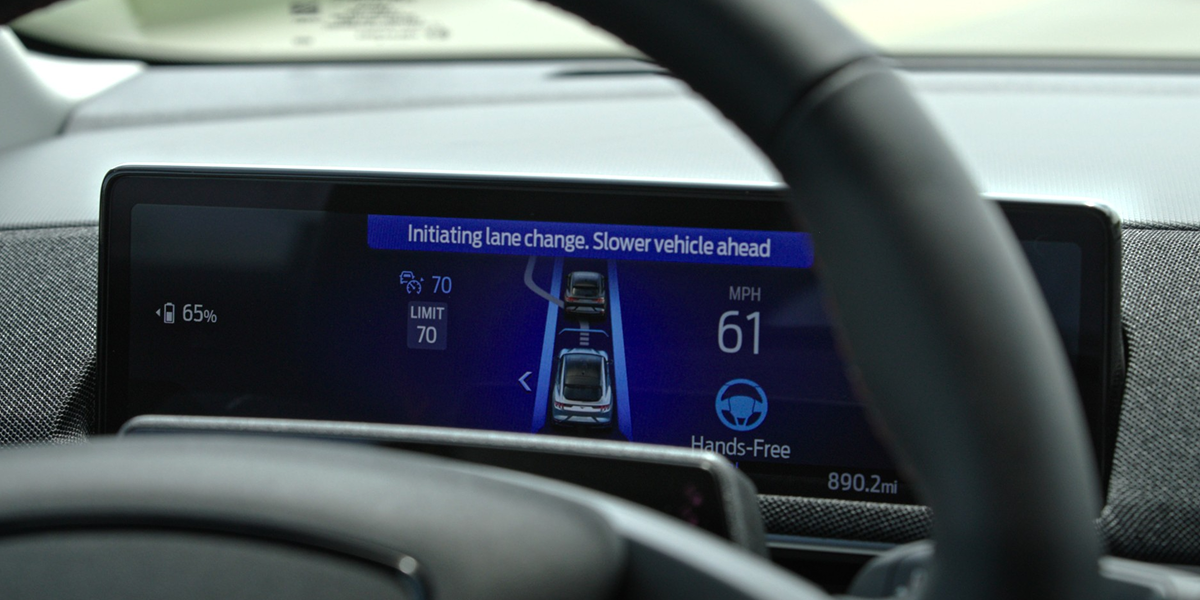 BlueCruise screen shown on a vehicle dashboard. Screen is
showing a visual of the vehicle in a lane, a 70 MPH speed limit, current speed
of 61 MPH, and reads "Initiating lane change. Slower vehicle ahead."