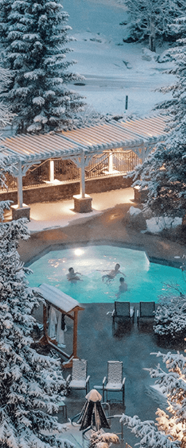 A group of friends swimming in a heated pool with snowy scenery around them.