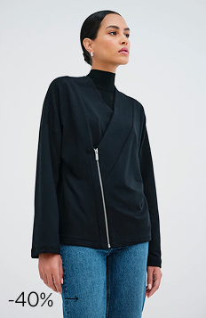 Astrid in The Tillary Sweatshirt Jacket with a diagonal silver zipper over a black turtleneck and blue jeans.
