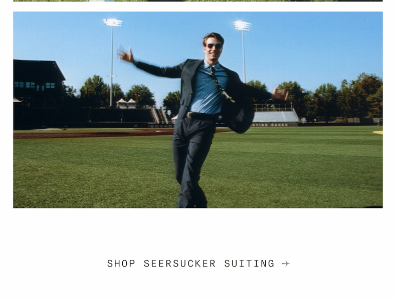 A smiling man runs joyfully across a baseball field in a dark seersucker suit and sunglasses. The sunny sky and stadium lights are visible behind him. Text below reads, “SHOP SEERSUCKER SUITING →”.
