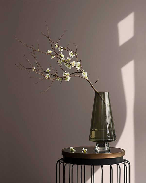 A taupe painted wall behind a table holding a vase of flowered branches.