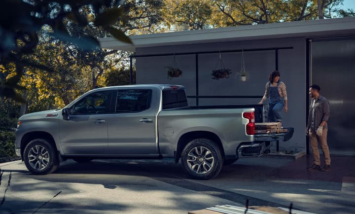 Chevy truck parked in front of a house; two people stand by the bed loaded with wood planks.