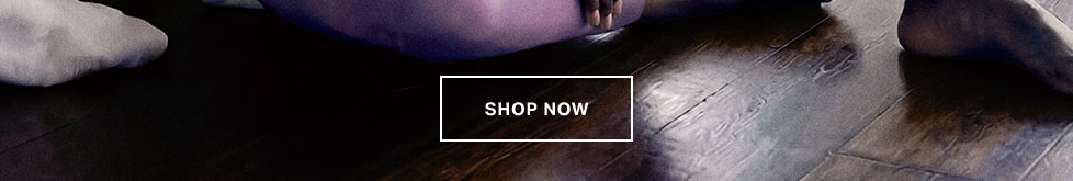 Woman in cozy purple loungewear sitting on a wooden floor with a 'SHOP NOW' button. Explore our new comfortable athleisure collection.