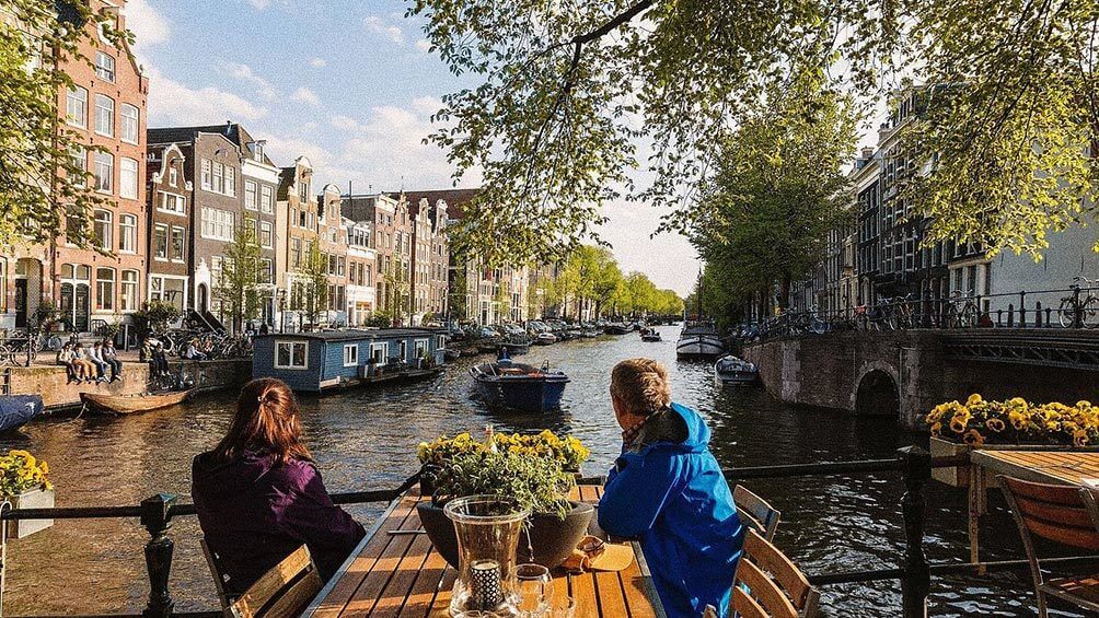 Image description: Couple sitting at table looking at canal in Amsterdam.
