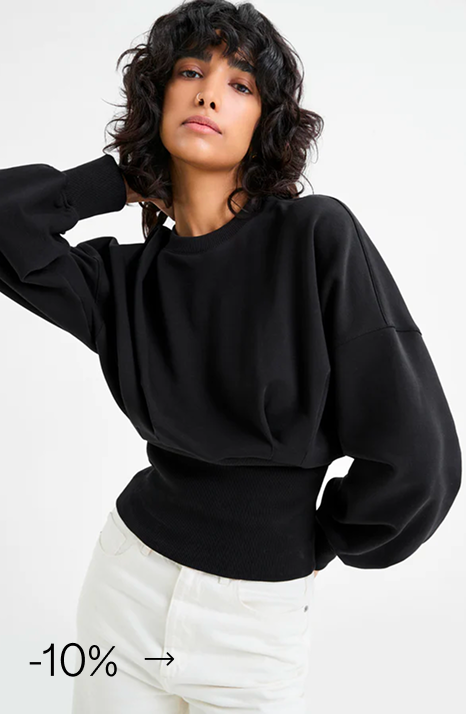 Emma in The Maris Sweatshirt - a black balloon-sleeve sweatshirt paired with white pants.