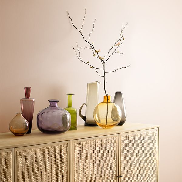 A pale neutral wall with a cabinet and decorations in front of it.