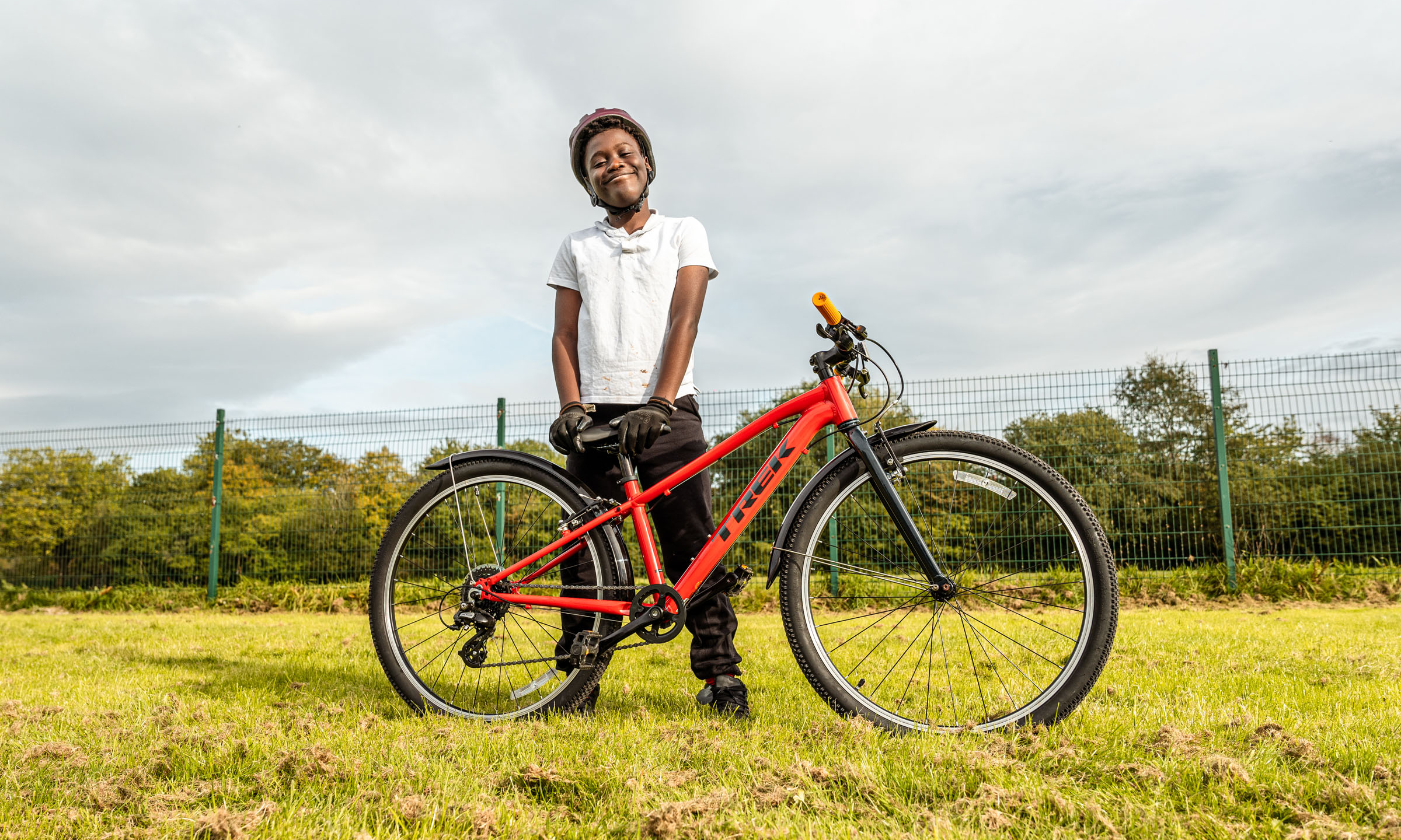 A boy standing with his bike on a grass field.