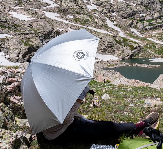 person sitting next to lake with umbrella