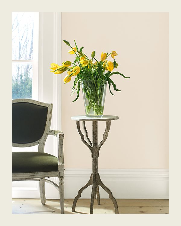 A small table topped with a vase of yellow tulips sits in front of a pink painted wall.