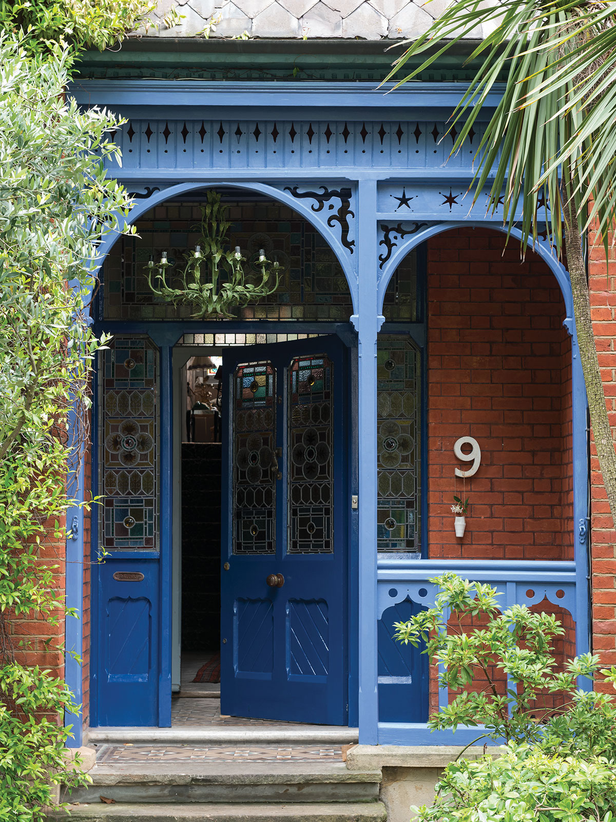 The open front door entices us to step onto this ornate porch with its bright blue, intricate woodwork. It’s the perfect contrast to the traditional red brickwork and lush verdant green plants that surround it. As you glance up, the light green many-branched porch light catches your eye, and then you notice the multi-coloured tones of the stained glass, all contributing to a bright and cheerful entranceway.