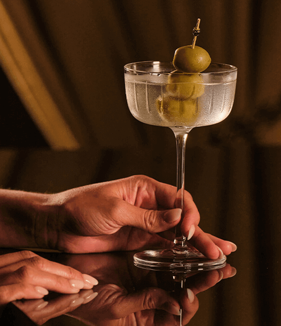 A hand holding a martini with olives.