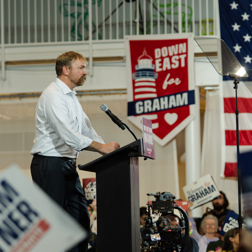 Graham Platner, seen from the side, stands behind a podium.