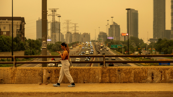 A woman is walking on a busy overpass against a smoky sky.