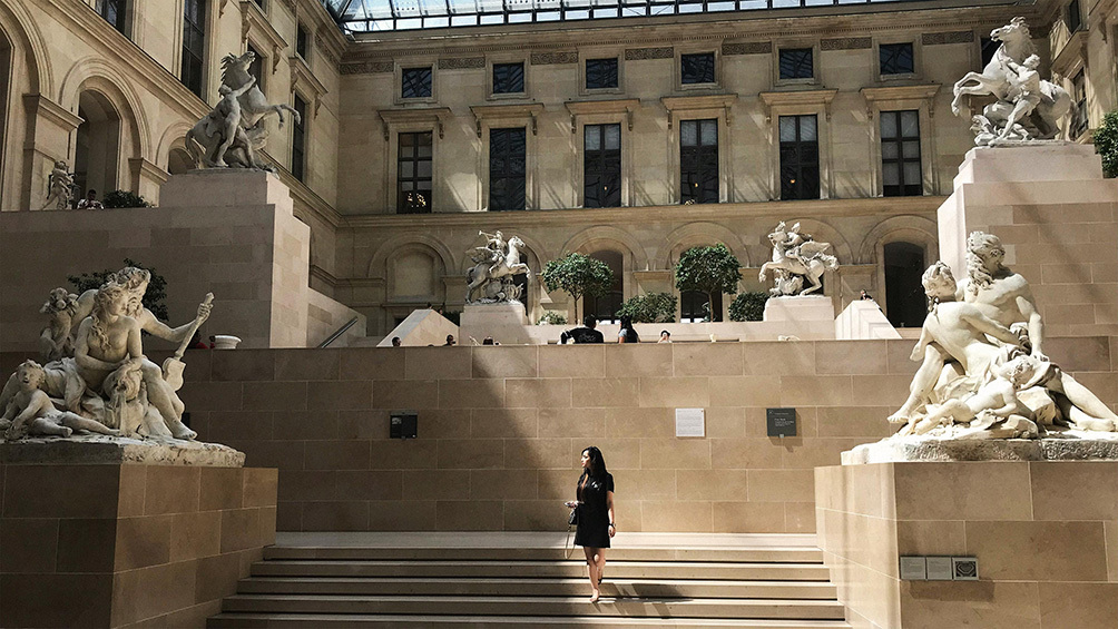Image description: Woman walking down stairs at the Louvre, in Paris.
