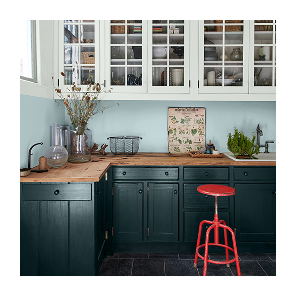 A modern farmhouse kitchen with light blue painted walls, white cabinets, dark green-painted lower cabinets and a red stool.