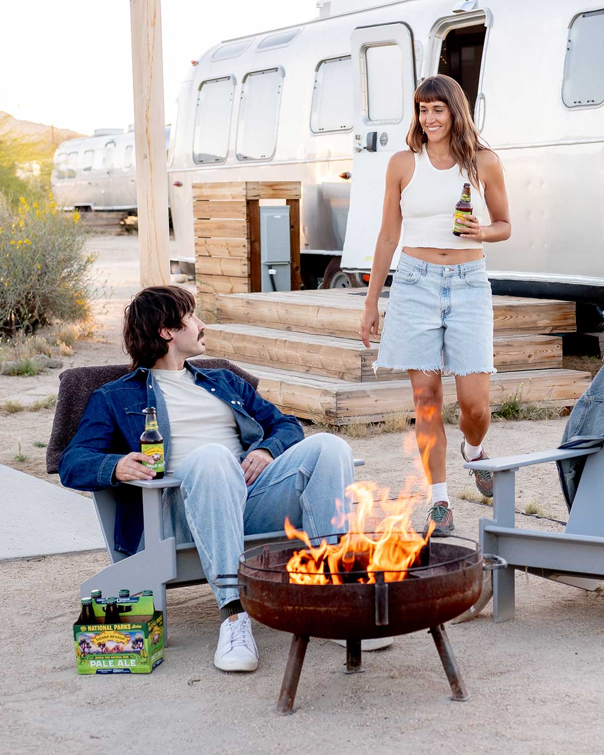 A young man and woman outside of an AutoCamp Airstream, holding bottles of Sierra Nevada Pale Ale