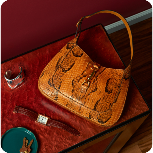 A handbag, a watch, and a cuff bracelet on a red table linking to selling on eBay