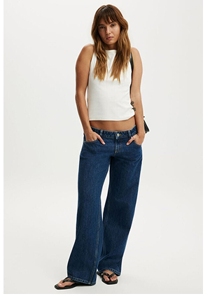 Woman wearing white sleeveless tank top and dark blue wide-leg denim jeans with black slide sandals