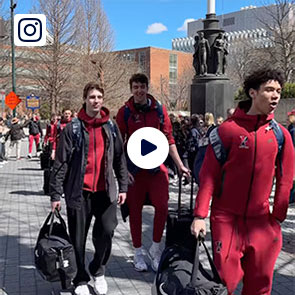 The men's basketball team walks through a courtyard towards a bus.