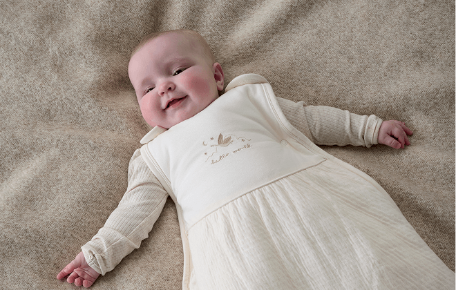 Baby lay, smiling, wearing duckling style dreampod sleep bag