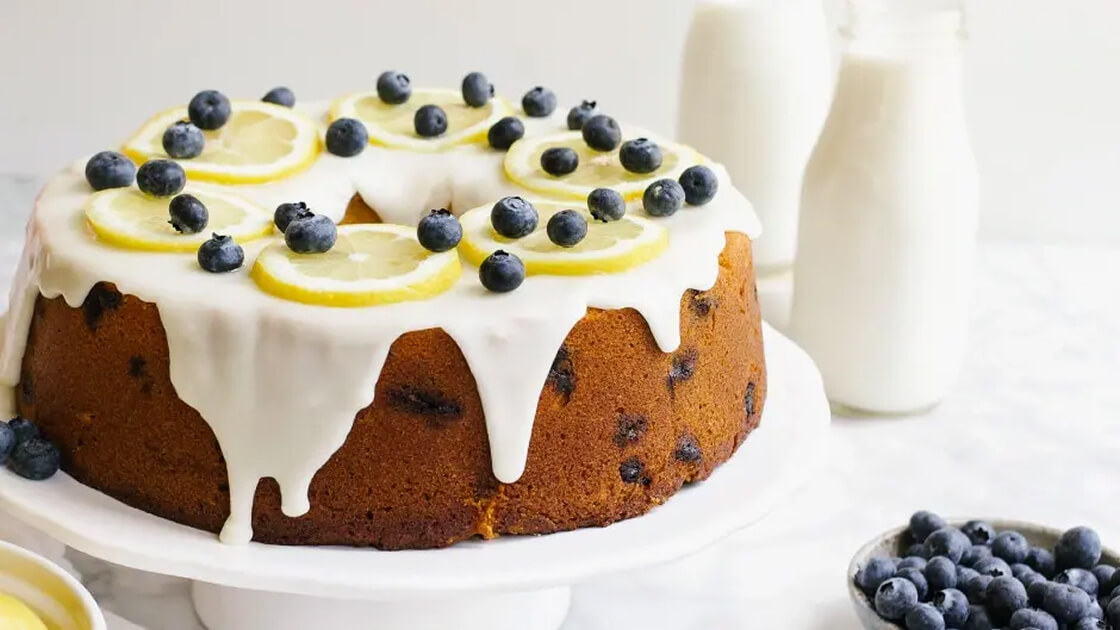 Close-up image of a cake with slices of lemon and blueberries on top.