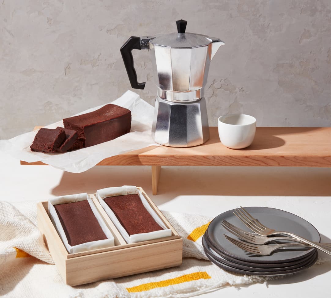 A Tokyo Gâteaux Duo and a single Gâteau next to plates, forks, an espresso maker, and a cup.