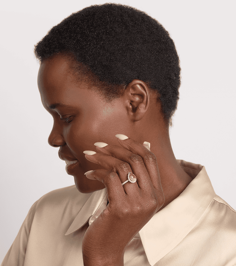 Close up of female model wearing a pear shaped citrine halo ring with diamond pavé band. Limor Touchstone logo. Click shop the collection.