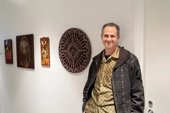 A man leans against a white wall next to three pieces of art.