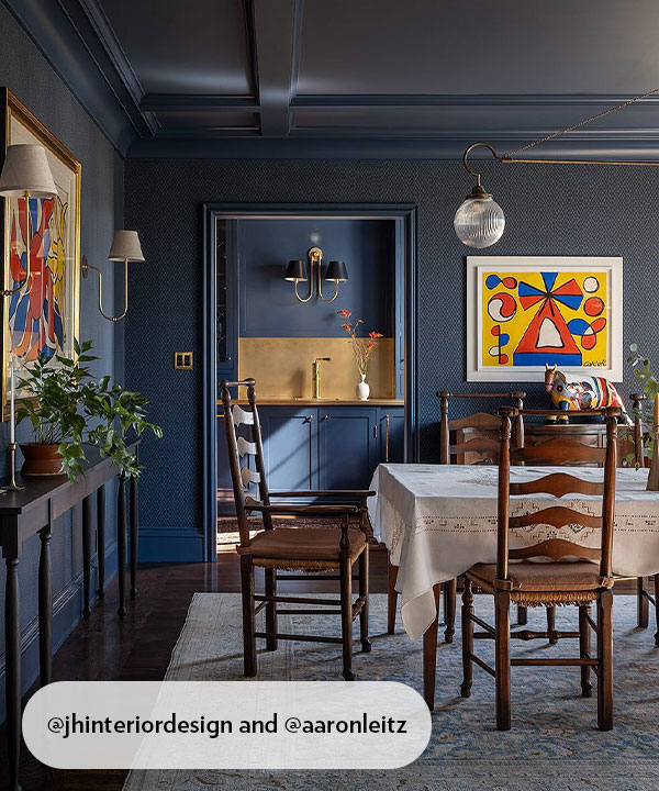 A dramatic navy dining room with a coffered ceiling, vintage wooden chairs, and bold abstract art. Warm brass accents and soft lighting add depth and richness, creating a space that feels both refined and warmly lived-in.