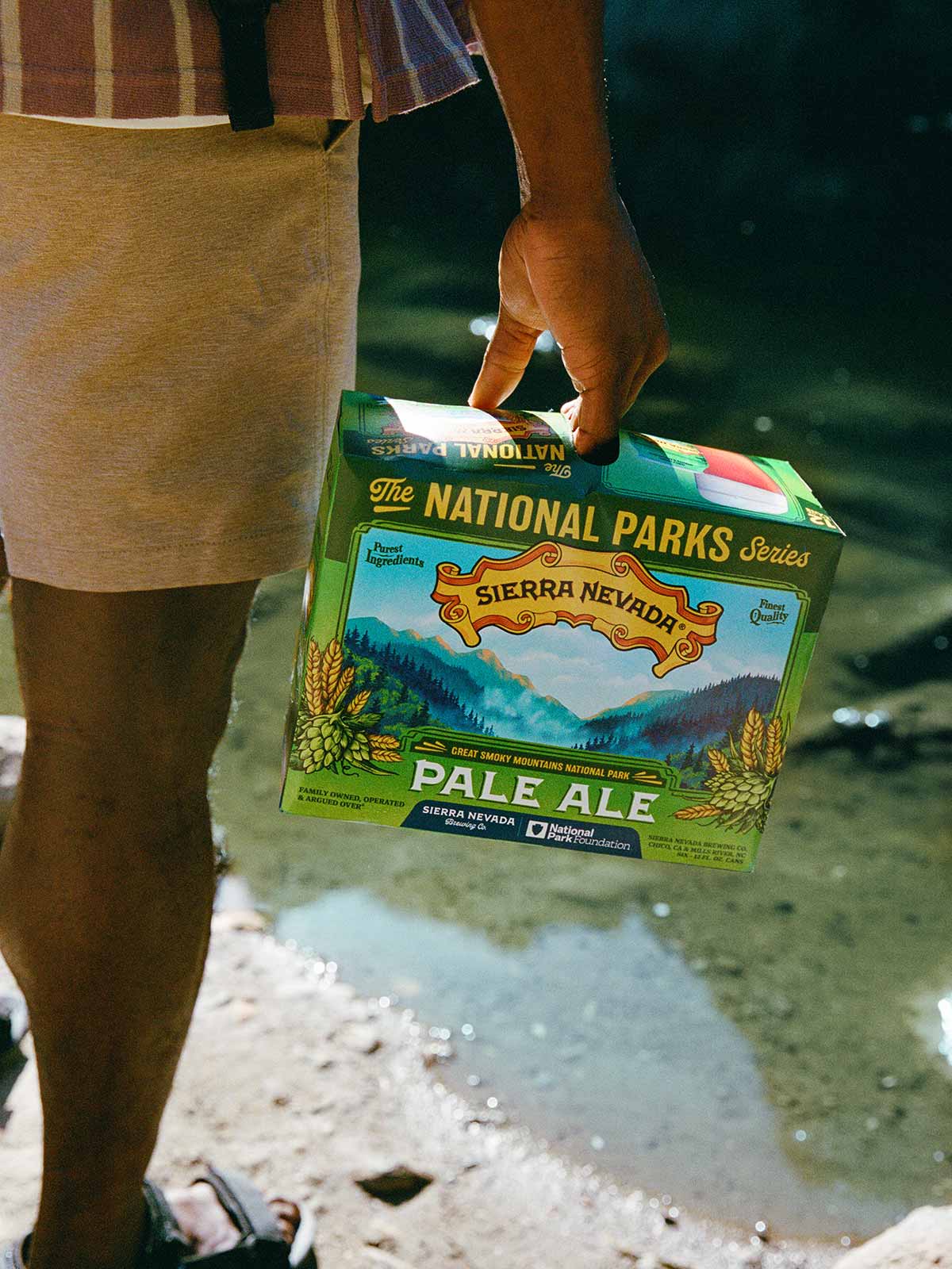 A man holding a 12-pack of Pale Ale next to water