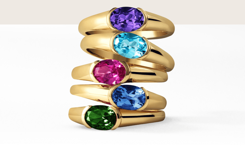 Stacked yellow gold dome gemstone rings featuring oval stones of different colors.