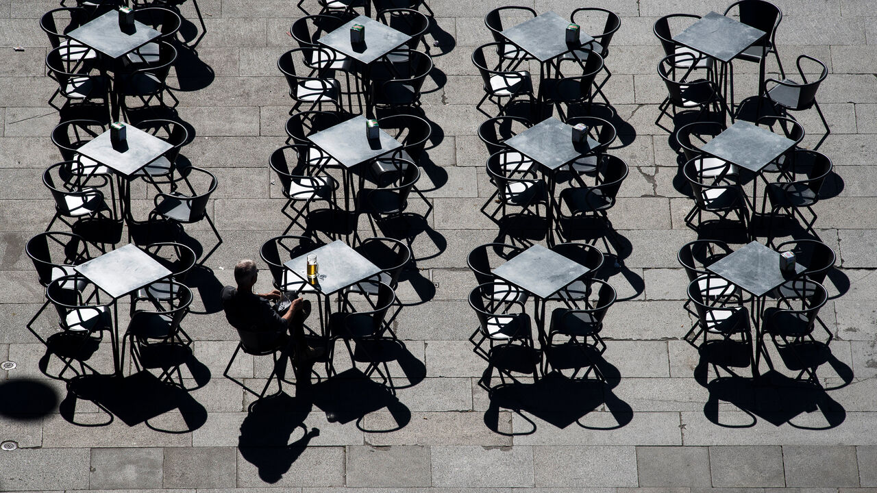 A lone man sits with a beer, at one of many cafe tables in a square in downtown Porto, Portugal.