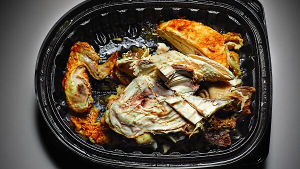 A partially eaten chicken dish in a black plastic takeout container.