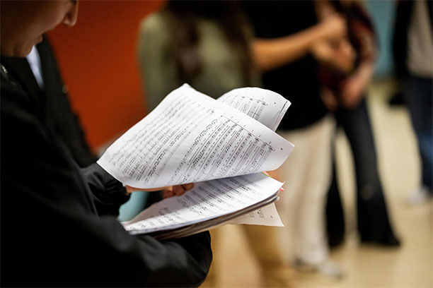 A student turns the page on a packet of sheet music.